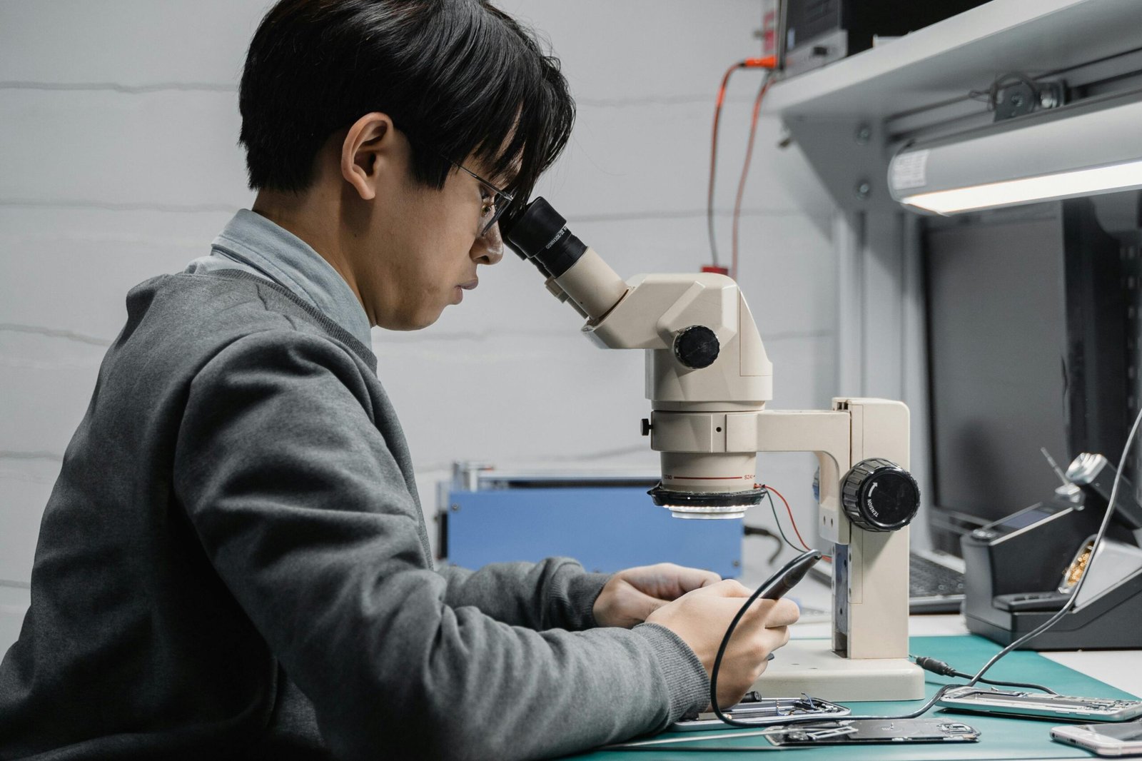 A focused technician repairing electronic components with a microscope in a lab.